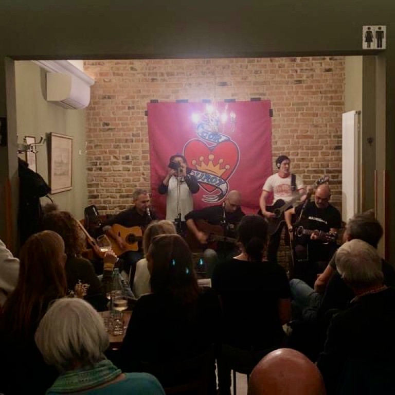 Corduroy im Glauburg Cafe, hinten die Band vor einer Backsteinwand, beleuchted von einem Kronleuchter, vorne Publikum von hinten gesehen durch den Raum