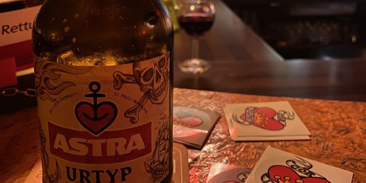 Corduroy Herz Logo Aufkleber auf Tresen, davor eine Flasche Astra Bier mit Herz/Anker Logo